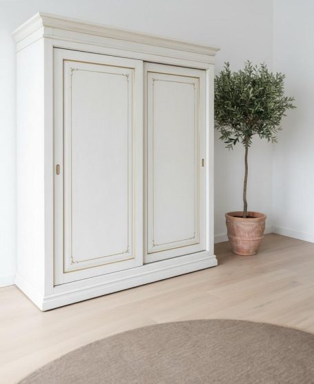 Weißer geschlossener Schrank neben einem Topf mit einer kleinen Pflanze auf dem Boden.