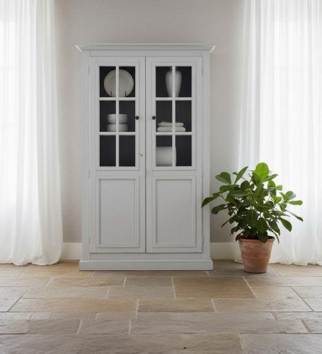 Weißer Vitrinenschrank mit Glasfront, neben einer Pflanze in einem Topf.