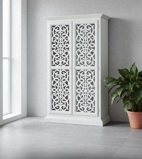 Weißer Schrank mit filigranem Muster neben einer Topfpflanze in modernem Raum.