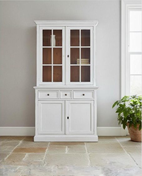 Weißer Schrank mit Glasfronten und zwei Schubladen, vor grainer Wand.