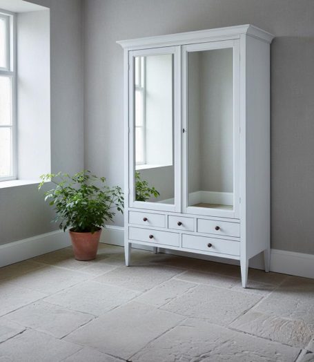 Weißer Kleiderschrank mit Spiegel und Schubladen, neben einer Pflanze in einem Topf.