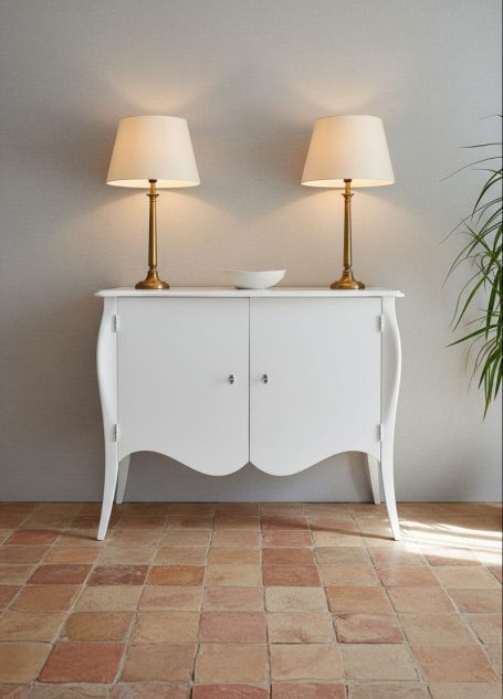 Weißer Sideboard mit zwei Lampen und einer Pflanze, vor einer grauen Wand.