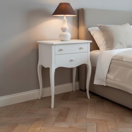 PR-4089 Weißer Nachttisch mit zwei Schubladen und einer Lampe neben einem Bett.