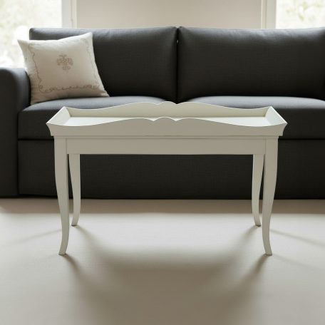 Weißer Couchtisch mit geschwungenen Beinen vor einem grauen Sofa und einem Kissen.